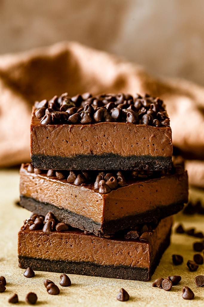 A square of rich, glossy no-bake chocolate cheesecake sitting on a dark plate, topped with mini chocolate chips—one of the easiest Chocolate Cheesecake Bars to make, showcasing a creamy Chocolate Cream Cheese filling in a chilled No Bake Bars treat from the world of Easy Chocolate Desserts and Cheesecake Bars, perfect for any Food Cakes collection.