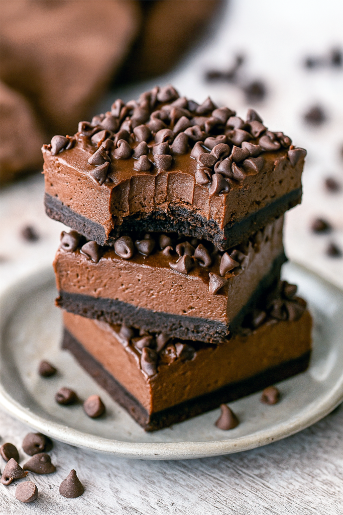 A square of rich, glossy no-bake chocolate cheesecake sitting on a dark plate, topped with mini chocolate chips—one of the easiest Chocolate Cheesecake Bars to make, showcasing a creamy Chocolate Cream Cheese filling in a chilled No Bake Bars treat from the world of Easy Chocolate Desserts and Cheesecake Bars, perfect for any Food Cakes collection.