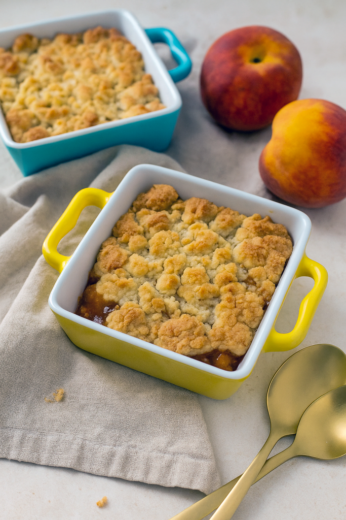 Two individual ramekins filled with bubbling peach cobbler, featuring golden-brown crumble topping and juicy peach slices.