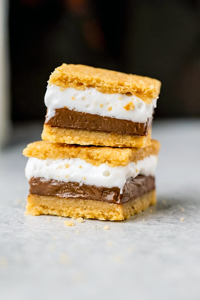 Close-up of broken s’mores cookie bars showcasing a golden graham cracker crust, marshmallow crème center, and melted chocolate, perfect for S’mores Dessert, Fall Bbq Desserts, S’mores Bites, Super Bowl Dessert Ideas, Smore Recipes, Cookie Bar Recipes, Yummy Sweets, Salty Snacks, and top Sweet Snacks Recipes.