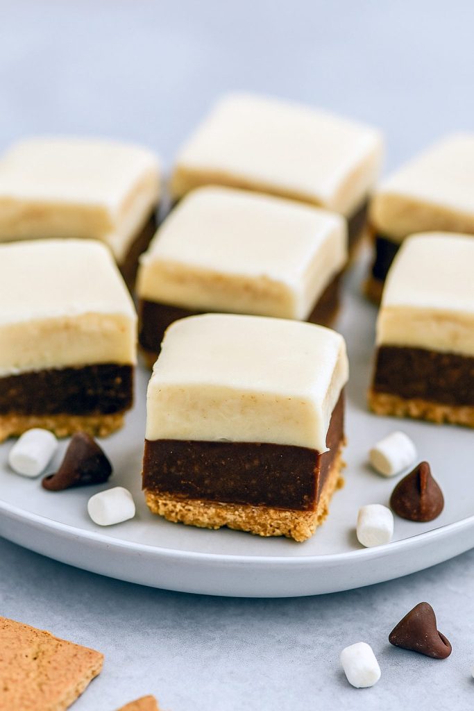 Square pieces of Smores Fudge stacked on a plate, showing chocolate, marshmallow, and graham cracker layers—an easy Layered Fudge from the best Fudge Dessert Recipes.