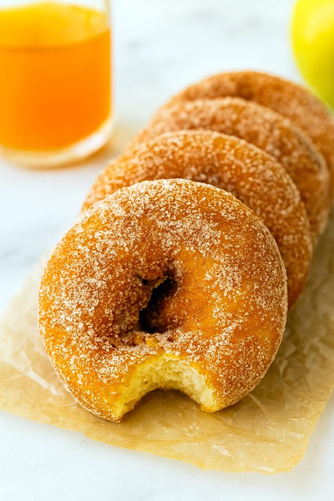 A dozen spiced apple cider–infused, cake-style donuts arranged on a cooling rack, each coated in cinnamon sugar and gleaming with autumn warmth.