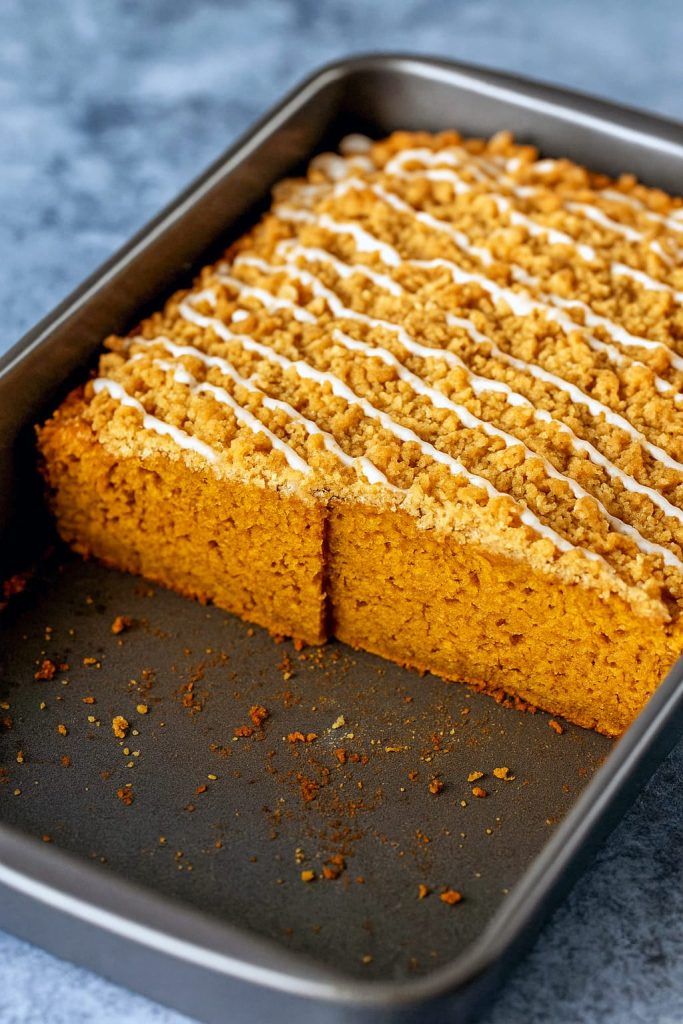 A square slice of pumpkin coffee cake with a golden crumb, topped with a chunky cinnamon streusel and drizzled with vanilla glaze.