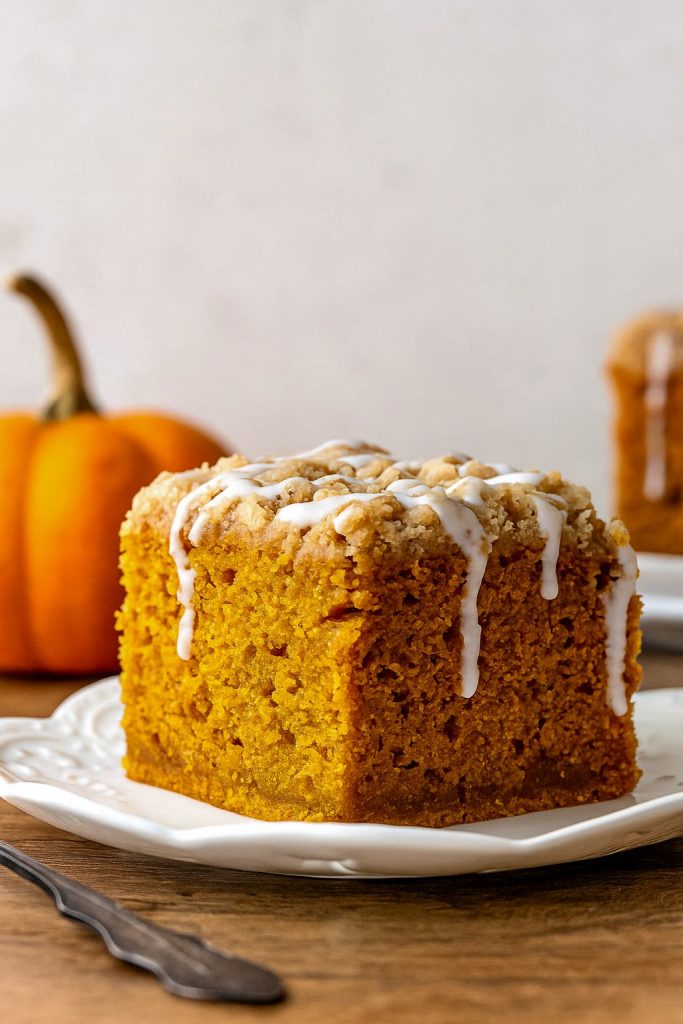 A square slice of pumpkin coffee cake with a golden crumb, topped with a chunky cinnamon streusel and drizzled with vanilla glaze.