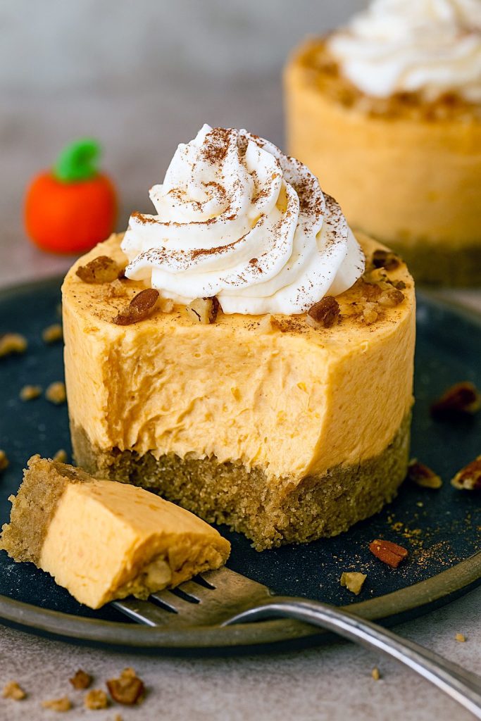 A row of mini no-bake pumpkin cheesecakes in paper cups, each showcasing creamy layers of Non Bake Pumpkin Cheesecake and Pumpkin Pie Cheesecake No Bake filling on a golden graham base, perfect for Easy Fall Deserts For A Party, Pumpkin Cheesecake For Two, Halloween Desserts No Bake, Thanksgiving Recipes Baking, Mexican Food Recipes Easy Dessert, and all your Fall Recipes Dessert Halloween cravings.