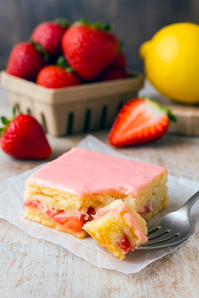 Two rosy-pink strawberry lemon blondie squares stacked, revealing the soft, moist interior studded with juicy berry bits and finished with a glossy citrus glaze.