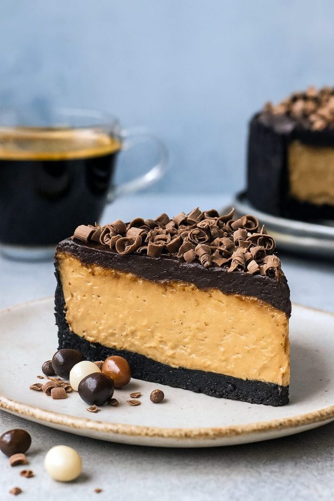 A slice of creamy coffee-infused cheesecake with an Oreo crust and chocolate ganache topping, served on a white dessert plate.