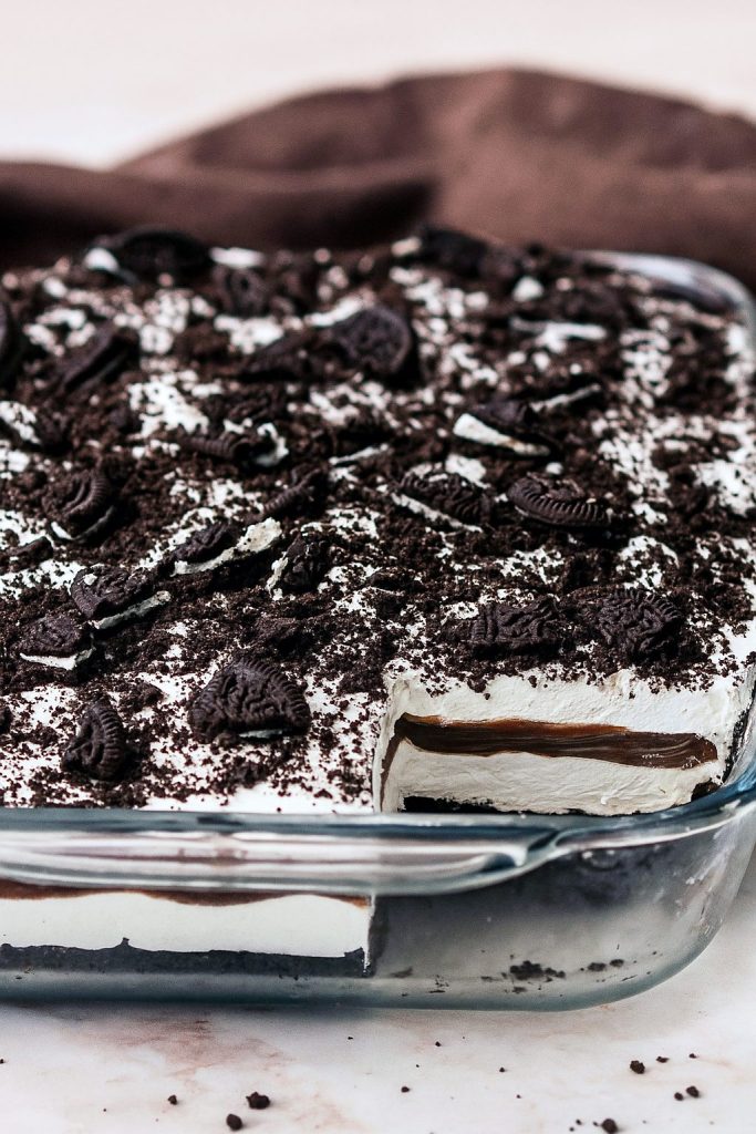 Close-up of chilled Oreo bars with a whipped topping, cookie crumb sprinkle and chocolate drizzle — a Striped Delight that gives major Dirt Pudding For A Crowd vibes, like an elevated Ding Dong Dessert crossed with a nostalgic Dirty Dessert.
