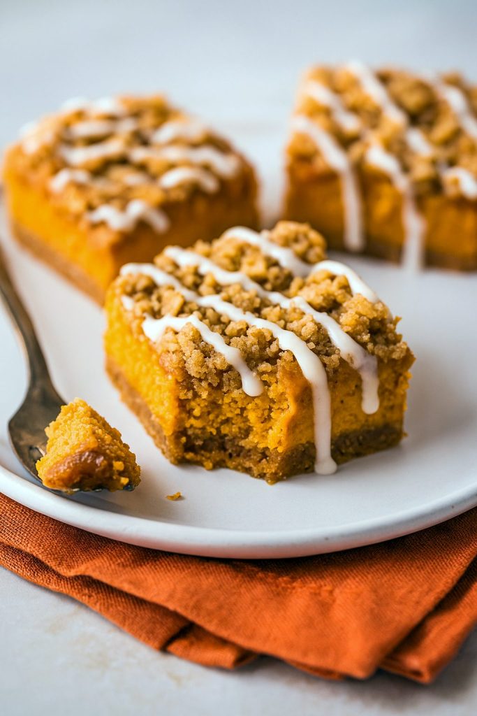 Overhead shot of a pan cut into Pumpkin Cheesecake Streusel Bars, each slice the texture of a mini Pumpkin Cheesecake Streusel Pie with a crisp gingersnap base reminiscent of Gingersnap Pumpkin Pie Bars or Pumpkin Pie Slab Bars, topped with a crumbly Streusel Bars layer, finished with a drizzle of Desserts Nutella, hinting at lighter Weight Watcher Desserts options, perfect as a play on Smores Dessert, packed full of Pumpkin Bars With Pumpkin Pie Spice flavor.