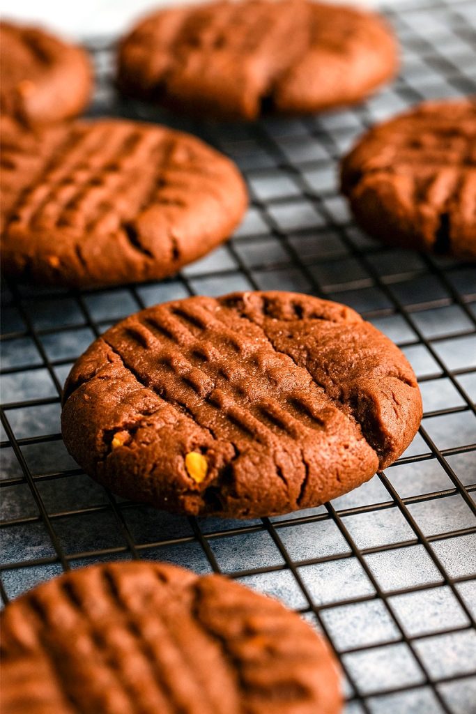Four thick, crisscross-patterned cookies featuring deep chocolate dough and swirls of peanut butter, cooling on a wire rack.