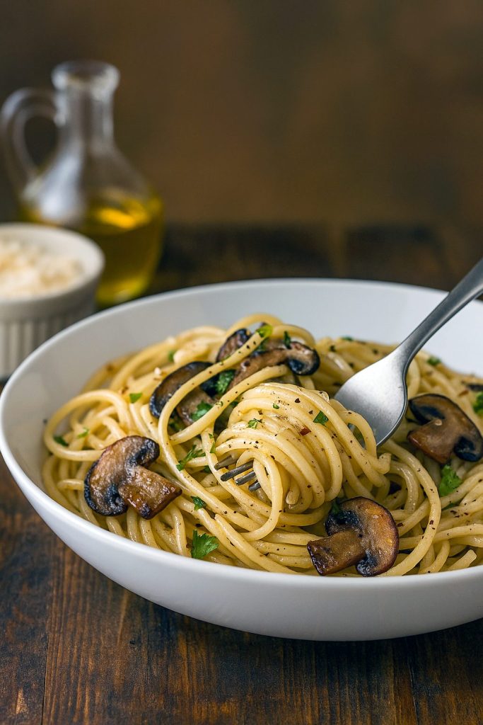 Close-up of spaghetti coated in a glossy mushroom and garlic sauce, topped with chopped parsley and grated Pecorino Romano.