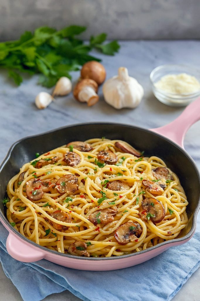 Close-up of spaghetti coated in a glossy mushroom and garlic sauce, topped with chopped parsley and grated Pecorino Romano.