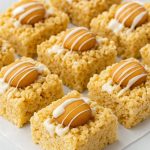 A close-up of gooey Banana Pudding Rice Krispy Treat bars topped with vanilla wafers, made using a Rice Krispie Treats With Banana Pudding Recipe, showing layers of crispy cereal and rich banana flavor—this Banana Pudding Rice Krispie Treats Recipe is easy to make and full of flavor. These Rice Krispie Treats With Banana Pudding are ideal for sweet tooth cravings, and the Banana Pudding Rice Krispie Treats are topped with a drizzle of white chocolate for an extra treat.