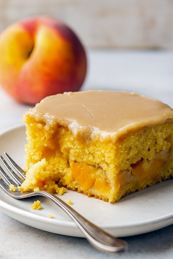 Slice of moist Peach Cake topped with rich brown sugar icing, loaded with Brown Sugar Peaches, and perfect for fans of Peach Cake Recipes and summery Peach Desserts. A must-try Peach Recipe and nostalgic USA Food favorite.