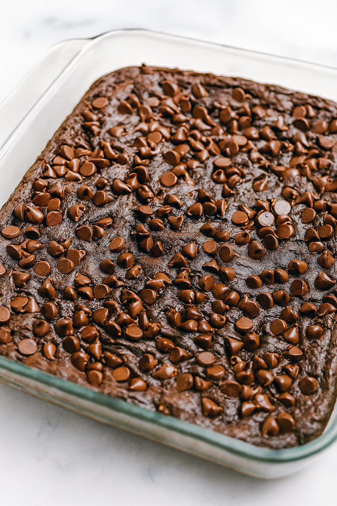 A warm, fudgy chocolate slab in a glass baking dish dotted with melted chocolate chips, showing the rich texture of a dump cake fresh from the oven.