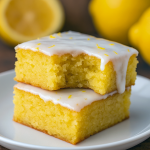 Close-up of gooey Lemon Cake Brownies topped with lemon glaze, cut into squares on a white plate, perfect for Fall Baked Recipes and Fresh Lemon Recipe Ideas.