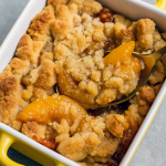 Two individual ramekins filled with bubbling peach cobbler, featuring golden-brown crumble topping and juicy peach slices.