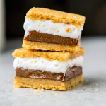 Close-up of broken s’mores cookie bars showcasing a golden graham cracker crust, marshmallow crème center, and melted chocolate, perfect for S’mores Dessert, Fall Bbq Desserts, S’mores Bites, Super Bowl Dessert Ideas, Smore Recipes, Cookie Bar Recipes, Yummy Sweets, Salty Snacks, and top Sweet Snacks Recipes.