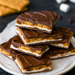 Irregular shards of s’mores bark studded with mini marshmallows, crushed graham crackers, and chocolate flakes on parchment, showcasing a no‑bake treat perfect for sweet snacking.