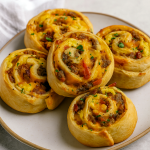 A wooden board piled with golden, crescent‑dough breakfast rolls stuffed with eggs, sausage, bacon, and cheese—an Easy Breakfast Platter that doubles as Quick Easy On The Go Breakfast, a festive Thanksgiving Breakfast Board, Brunch To Go Ideas, Breakfast Party Finger Foods, Make Ahead Grab And Go Breakfast, Breakfast Ideas For Working Men, Group Breakfast Ideas Make Ahead, and Filling Breakfast Ideas On The Go.