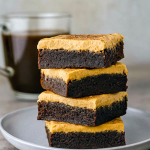 A square mocha brownie topped with café‑latte frosting and marshmallow swirls, set against a rustic wooden backdrop.