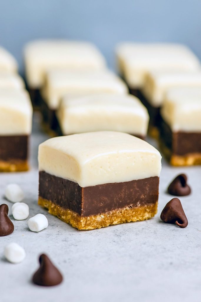 Square pieces of Smores Fudge stacked on a plate, showing chocolate, marshmallow, and graham cracker layers—an easy Layered Fudge from the best Fudge Dessert Recipes.
