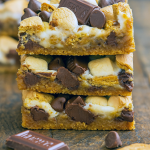 Golden-brown seven layer s’mores bars in a pan with toasted marshmallows and melted chocolate, cut into square servings on a parchment-lined baking dish.