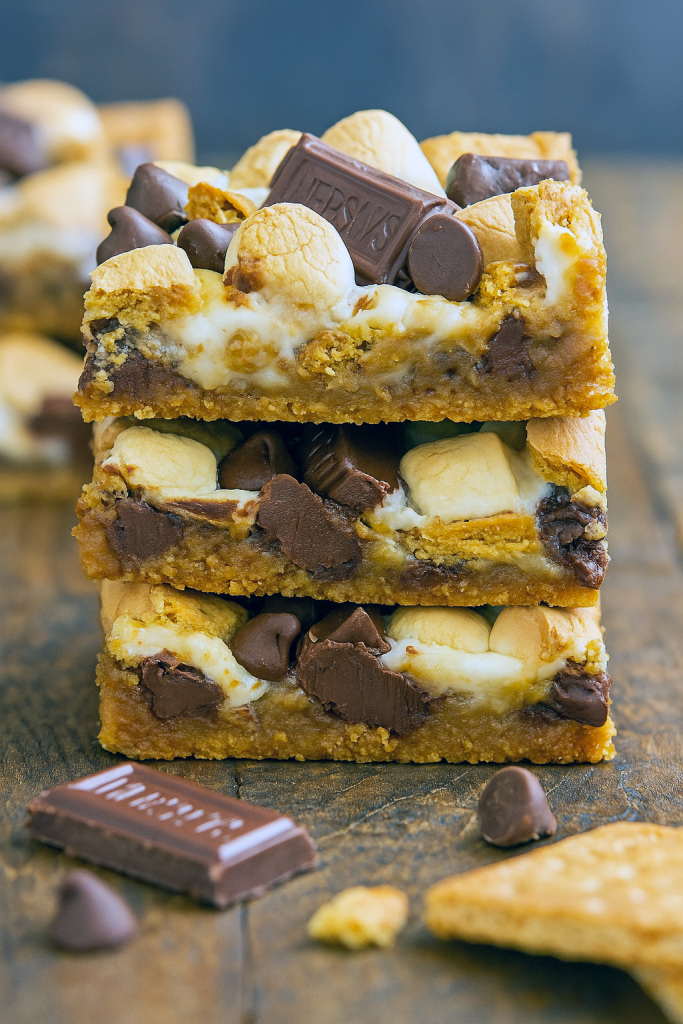Golden-brown seven layer s’mores bars in a pan with toasted marshmallows and melted chocolate, cut into square servings on a parchment-lined baking dish.