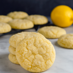A cooling rack filled with soft, round lemon cookies dusted in lemon sugar, each topped with a light lemon glaze, showcasing a bright yellow hue and fluffy texture.