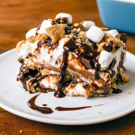 A 9×9 pan filled with layered no‑bake dessert, showing alternating stripes of chocolate pudding, peanut butter filling, and marshmallow cream topped with mini marshmallows and chocolate chips—an irresistible S’mores Lasagna Dessert, also described as Peanut Butter S'mores Cake, No Bake Chocolate Peanut Butter Lasagna, Reese’s Chocolate Peanut Butter Cup Lasagna, and even Peanut Butter Cookie Lasagna, perfect for No Bake Summer Desserts, S'mores, Baking Sweets, and Yummy Sweets.