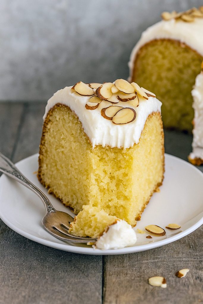 Rich and moist Amaretto Pound Cake topped with almond cream cheese frosting and slivered almonds, shown sliced on a plate with golden edges.