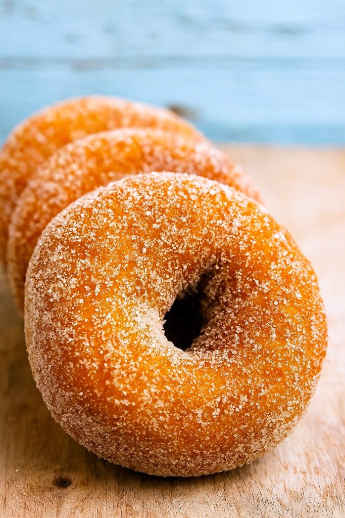 A dozen spiced apple cider–infused, cake-style donuts arranged on a cooling rack, each coated in cinnamon sugar and gleaming with autumn warmth.
