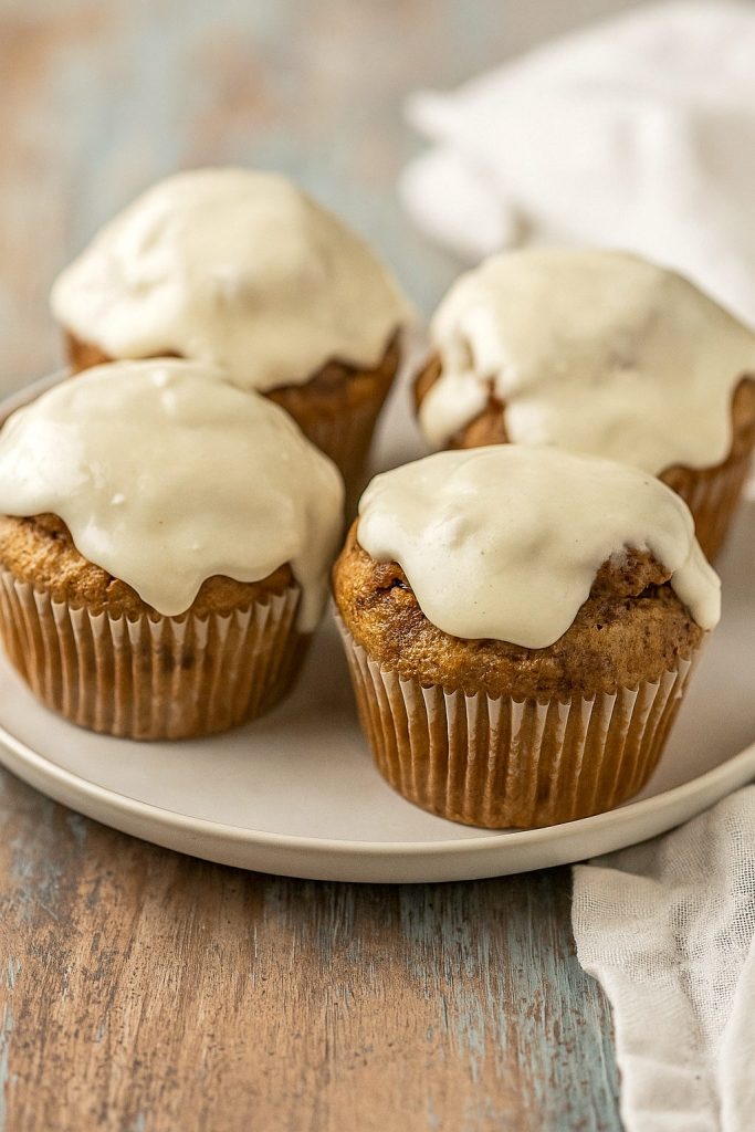 Close-up of soft and fluffy Muffins With Icing, swirled with cinnamon sugar and topped with Muffins With Cream Cheese Frosting, perfect for brunch, dessert, or Baking Homemade treats like Cinnamon Bun Muffins and Muffin Cinnamon Rolls from the best Cinnamon Roll Muffin Recipes.