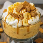 Trifle bowl with alternating layers of creamy vanilla pudding, banana slices, crushed Biscoff cookies and glossy caramel drizzle, topped with cookie crumbs.