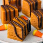 Glossy square pieces of fudge studded with candy corn pieces, arranged on parchment paper and ready to serve.