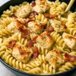 White bowl filled with rotini pasta coated in creamy ranch sauce, topped with grilled chicken strips and crispy bacon bits.