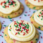 Festive stack of soft, round cake batter cookies generously coated in red, green, and white sprinkles, each topped with a swirl of buttery frosting, arranged on a holiday-themed plate.