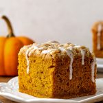 A square slice of pumpkin coffee cake with a golden crumb, topped with a chunky cinnamon streusel and drizzled with vanilla glaze.