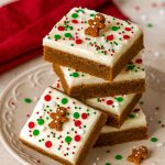 Frosted gingerbread bars on a holiday platter, topped with tiny gingerbread cookies and sprinkles, ready to serve.