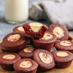 A dozen bite-size red velvet cheesecake cups with creamy white centers arranged on a decorative tray, each topped with a swirl of cheesecake filling.