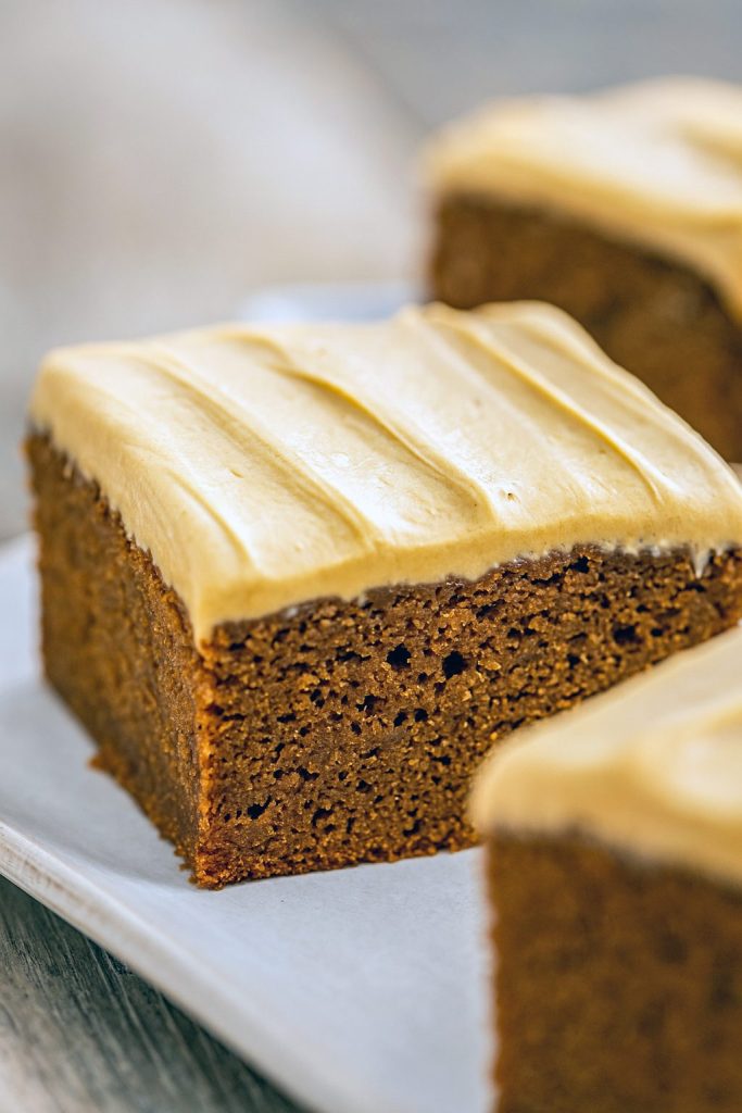 A moist, spiced Gingerbread Cake topped with creamy molasses frosting on a white plate, perfect for cozy Holiday Baking and festive Christmas Baking.