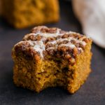 A square of pumpkin spice coffee cake topped with golden brown pecan streusel and drizzled with maple glaze, set on a rustic wooden table.