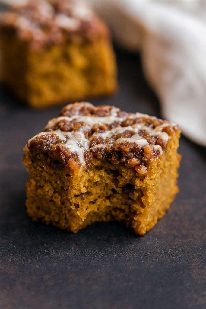 A square of pumpkin spice coffee cake topped with golden brown pecan streusel and drizzled with maple glaze, set on a rustic wooden table.