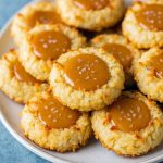 Plate of Thumbprint Cookies coated in coconut, topped with rich Coconut Caramel filling, evoking the creaminess of a Budino Recipe and the texture of a Culinary Hill Pizzelle, showcasing a Thumbprint Cookies Recipe that yields the best Caramel Cookies. These Coconut Cookies are Delicious Cookie Recipes brought to life, perfect for Cooking Classy treats.
