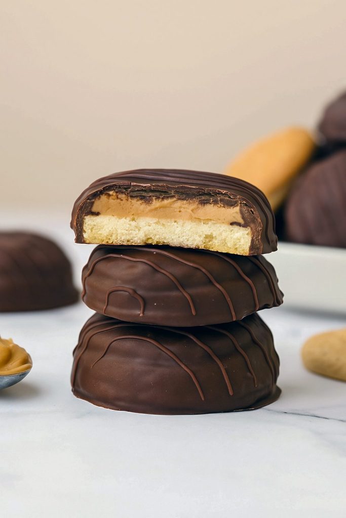 Close-up of Tagalong Cookies stacked in a tower with a visible Peanut Butter Filling layer inside, coated in glossy chocolate. This Stack Of Homemade Peanut Butter Cookies is perfect for fans of Girl Scout Cookie Types and Peanut Butter Filled Chocolate Cookies, showcasing rich Peanut Butter Cookie Filling and made for anyone who loves Yummy Cookies and Baking Sweets.
