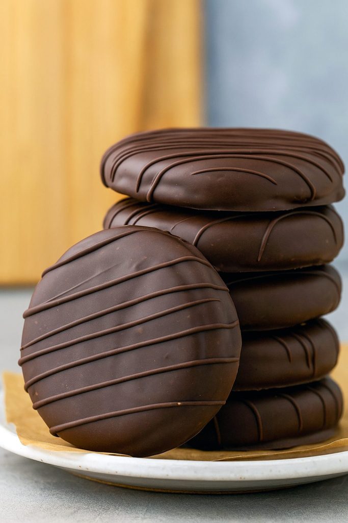 Close-up of Tagalong Cookies stacked in a tower with a visible Peanut Butter Filling layer inside, coated in glossy chocolate. This Stack Of Homemade Peanut Butter Cookies is perfect for fans of Girl Scout Cookie Types and Peanut Butter Filled Chocolate Cookies, showcasing rich Peanut Butter Cookie Filling and made for anyone who loves Yummy Cookies and Baking Sweets.