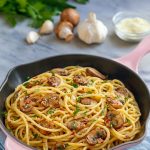 Close-up of spaghetti coated in a glossy mushroom and garlic sauce, topped with chopped parsley and grated Pecorino Romano.